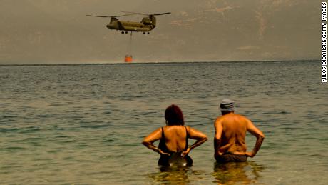 Anwohner beobachten, wie ein Chinook-Hubschrauber der griechischen Armee Wasser sammelt, während Feuerwehrleute am Sonntag in der Nähe des griechischen Dorfes Lambiri weiter gegen ein Lauffeuer kämpfen.