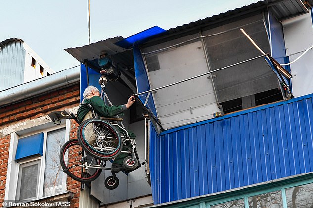 Herr Yudin erreicht sein Haus am oberen Ende des Aufzugs, indem er eine Tür zu seinem Balkon öffnet und seinen Körper und seinen Rollstuhl schwingt, um hineinzukommen