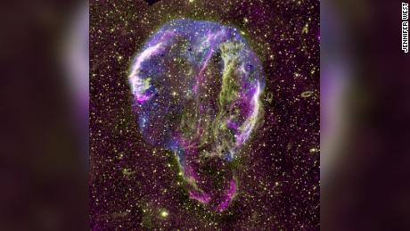 Gezeigt wird ein zusammengesetztes Radio- (lila), UV- (gelb) und Röntgenbild (blau) des Cygnus-Loop-Supernova-Überrests in der Milchstraße. 