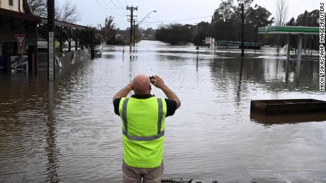 Ein Anwohner fotografiert am Sonntag, den 3. Juli 2022, eine von Hochwasser überschwemmte Straße in Camden im Südwesten Sydneys.