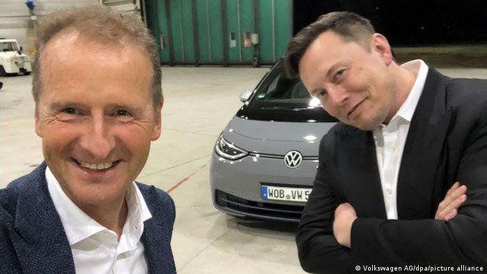 Herbert Diess und Elon Musk posieren für ein Selfie vor einem VW-Auto