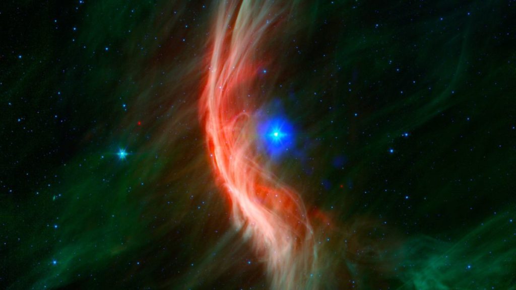 A bright blue star can be seen in deep space, surrounded by clouds of red gas.
